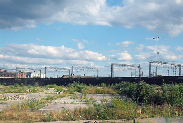 A large, unused, urban brownfield site with open land covered in cracked, overgrown concrete awaiting development in Leeds, England. © Adobe Stock, 282946502.