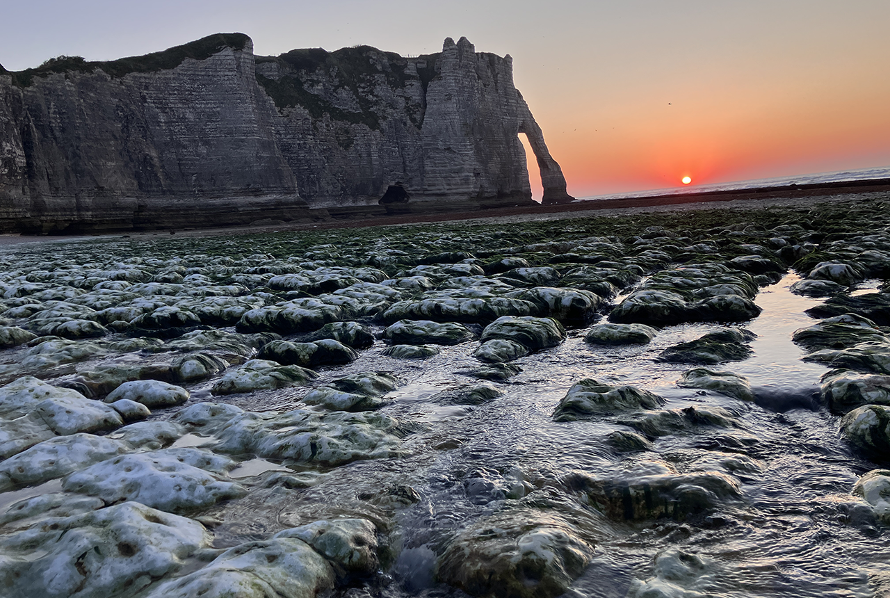 The sun setting behind the famous chalk arches at Étretat, France, with a significant karstic spring in the foreground. BGS © UKRI 2025.